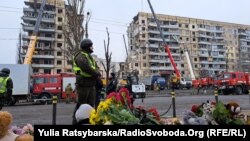 Людзі нясуць кветкі, зьнічкі і цацкі да будынку, зруйнаванага ў Дніпры ў выніку расейскага ракетнага ўдару. 16 студзеня 2023 году